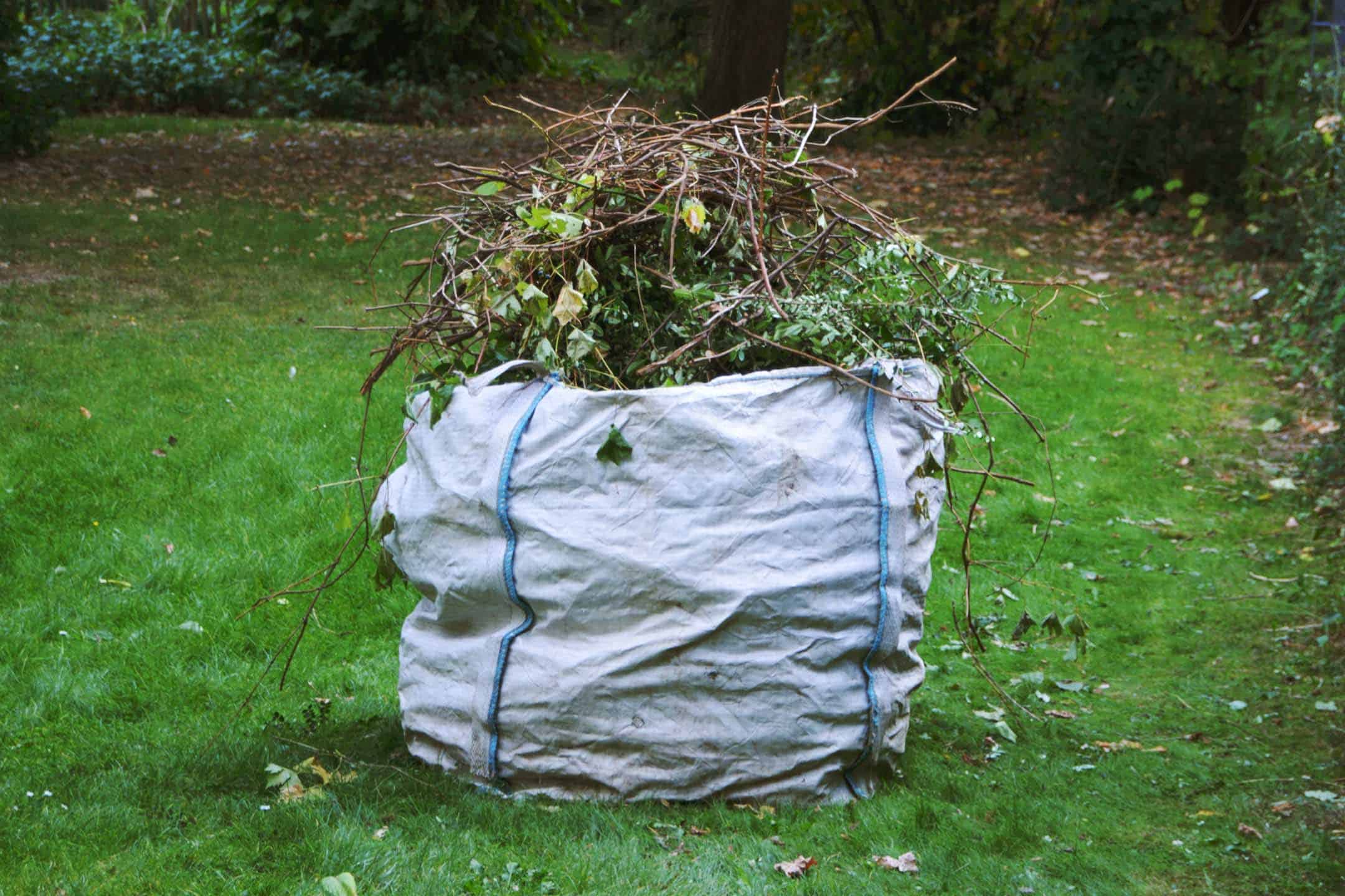 Large bag of garden waste overflowing from the top in the middle of a garden.